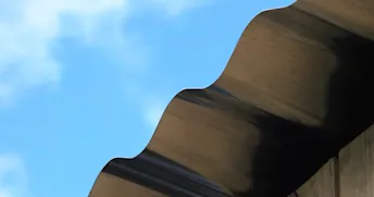 plattak-solceller.jpeg Kanten av ett grått plåttak med blå himmel i bakgrunden.