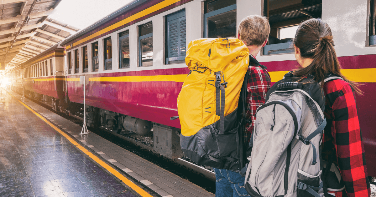 En kille och en tjej med stora ryggsäckar tittar på ett tåg som står vid perrongen.
