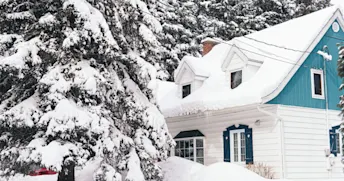 Snö på tak Vitt hus omgivet av snötäckta granar.