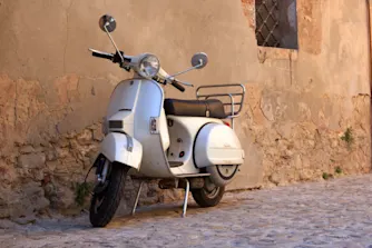 Halvförsäkring moped Vit vespa parkerad mot en tegelvägg.