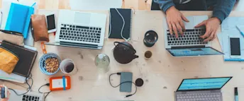 Egenföretagare datorer Flera datorer ligger på ett bord med te- och kaffekoppar, mobiler och andra saker runt omkring.