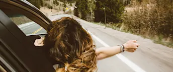 varldens-snabbaste-bil.jpg En kvinna lutar sig ut genom fönstret på en bil som kör fort längs en landsväg.