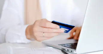 Black friday Hand som håller i ett blått kreditkort framför en laptop.