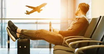 inställt-flyg.png Man sitter på flygplats och tittar på ett flygplan som lyfter.