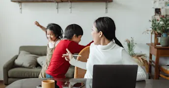 så mycket kostar ett barn.png Mamma som sitter vid datorn samtidigt som två barn leker.