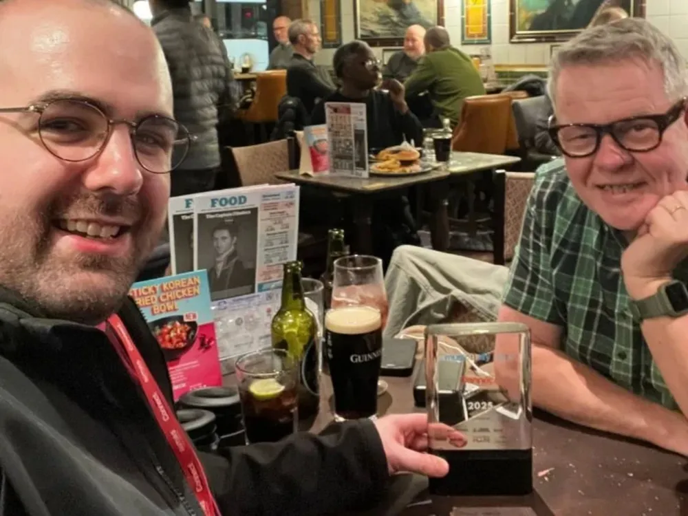 Two men, Dave Powell and Craig, celebrate with beers at a table after a successful conference.