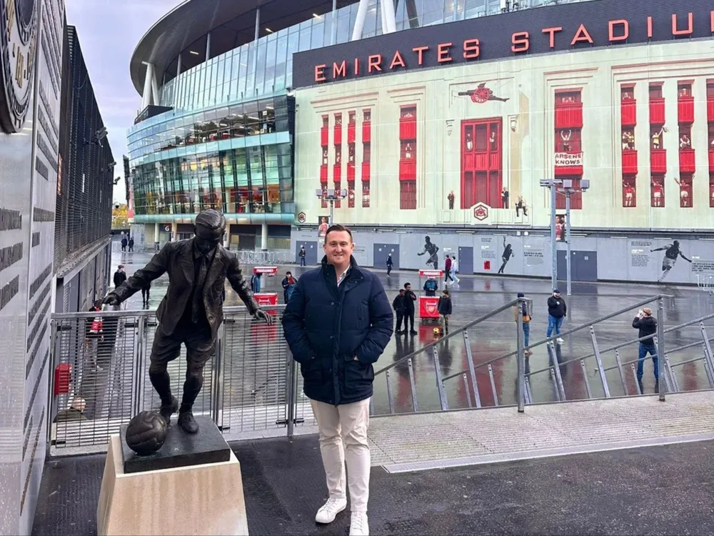 Dan stands proudly in front of a statue with Emirates Stadium in the backdrop, showcasing a memorable visit.