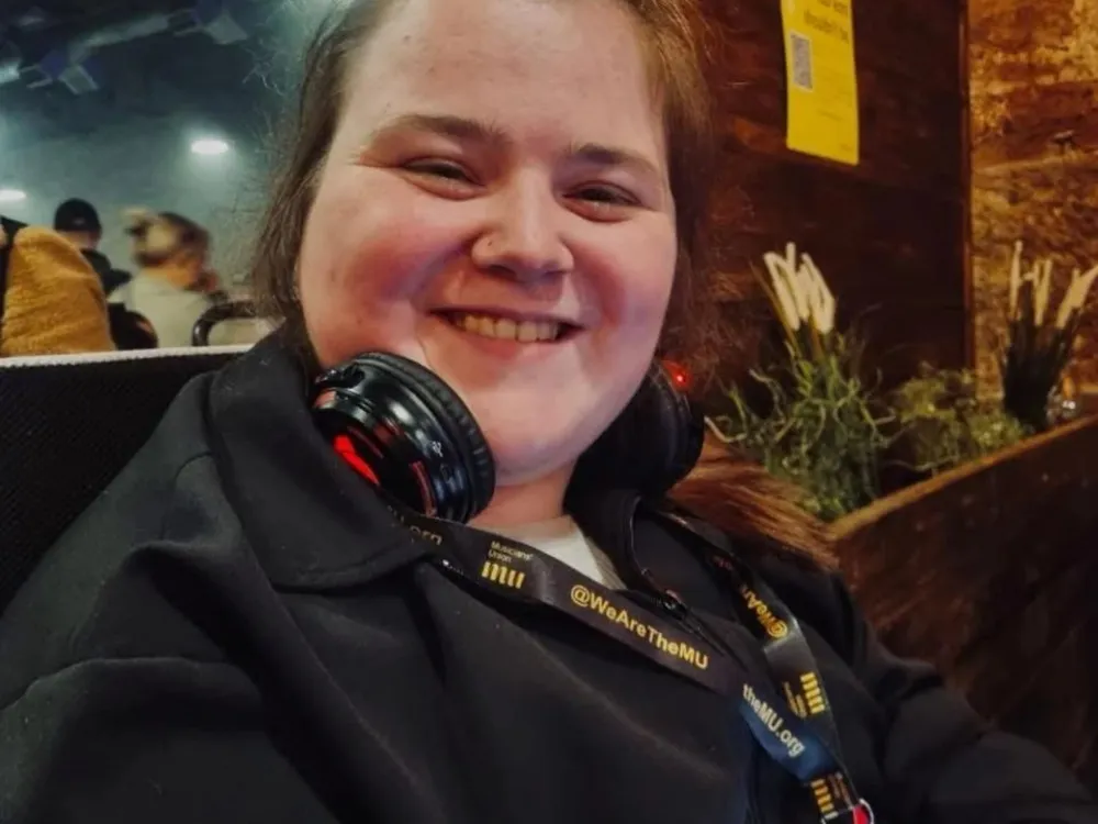 A smiling Niamh wears headphones, looking directly at the camera with a joyful demeanour.