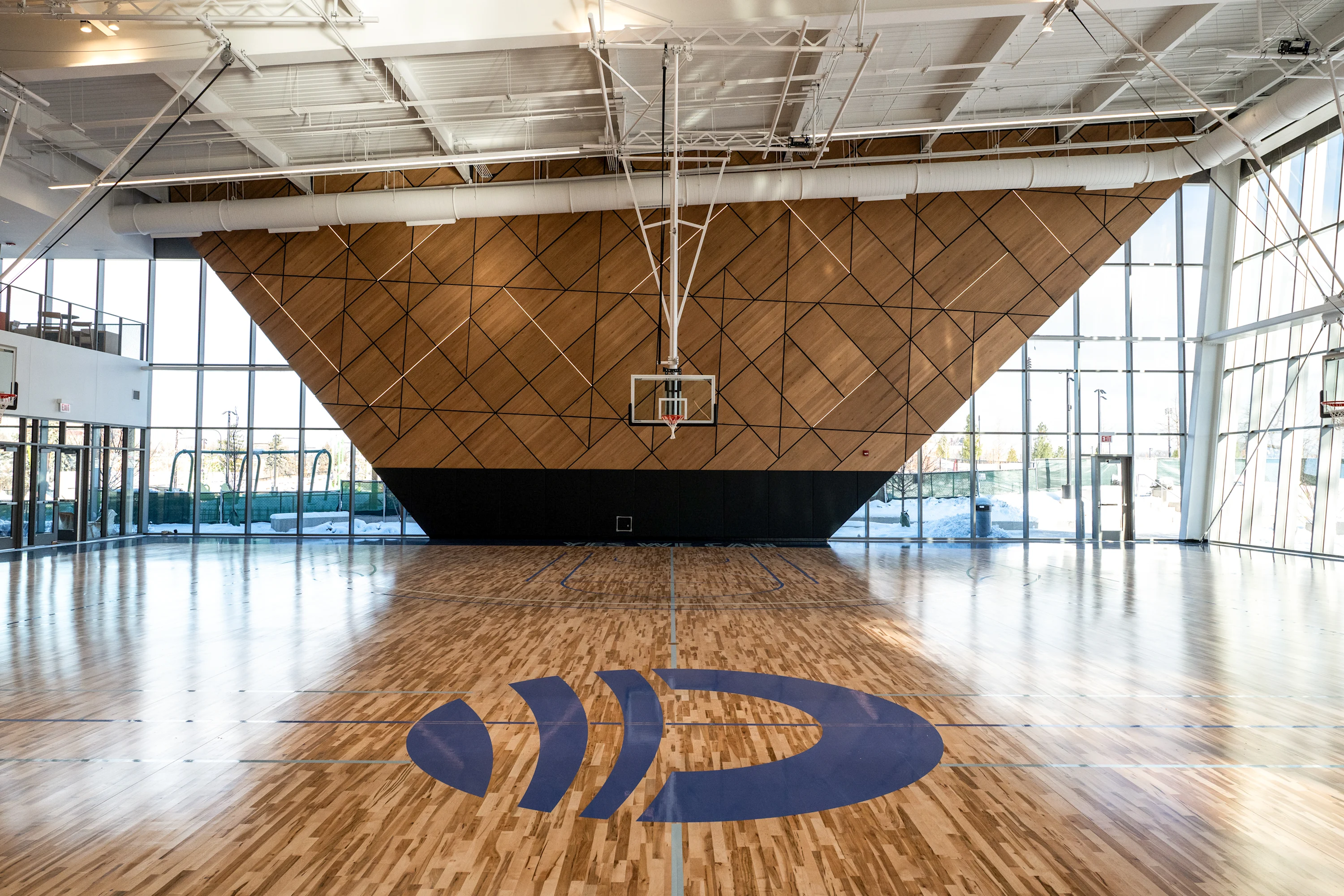 An image of Main Court, the basketball court located in Home Court. The image features the wood net-themed basketball backboard, the basketball net, and the basketball court floor.