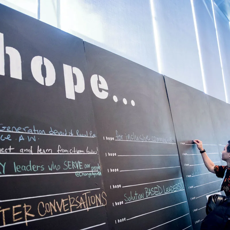 An Obama Foundation Summit participant writes down his thoughts on a large chalkboard with the words "I Hope..." written across the top.