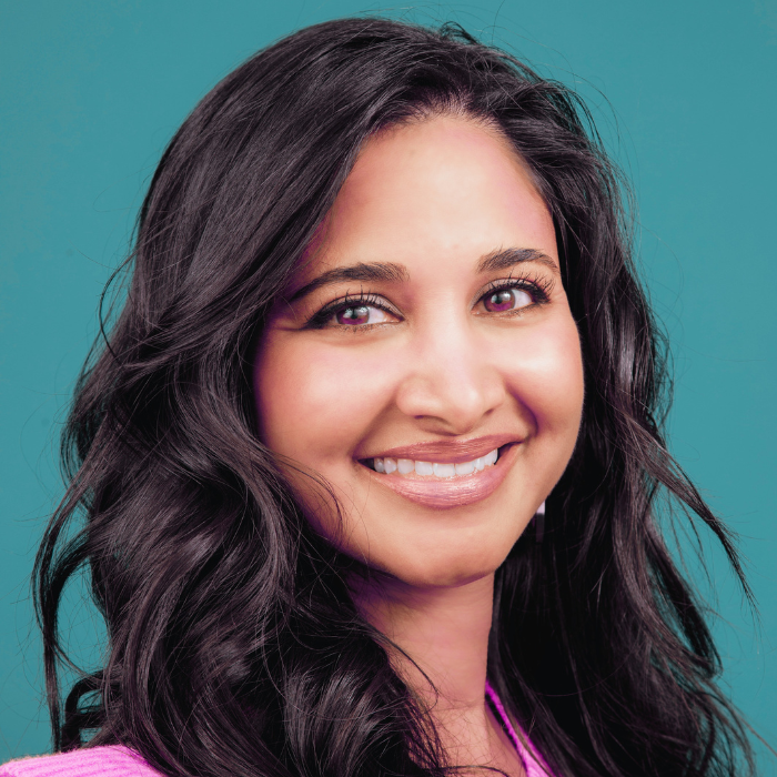 Jothsna Harris, an East Indian woman with a medium skin tone and curly black hair, smiles at the camera. 