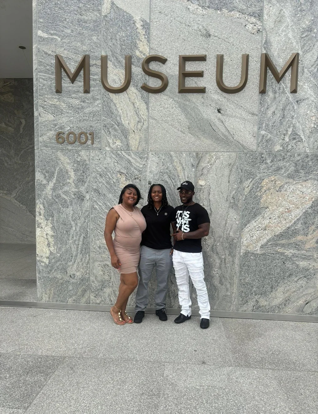 Toryn Parks, a Black woman with a medium skin tone and locs, poses with her parents, a Black woman with a medium skin tone and a Black man with a dark skin tone, in front of the Obama Presidential Center Museum Building sign.