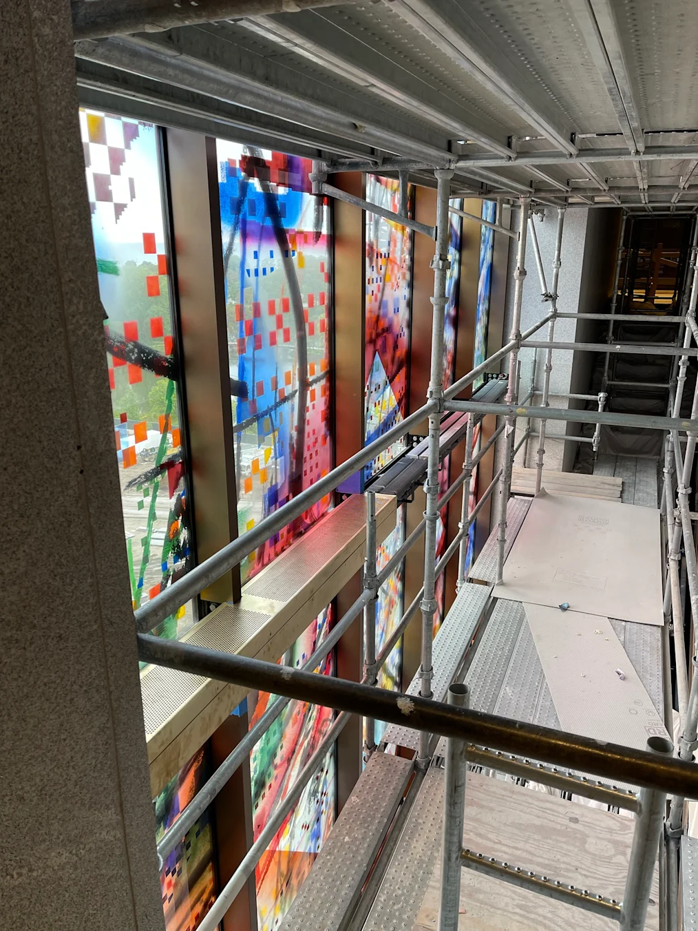 The image is a candid image of construction of the interior of the Obama Presidential Center Museum. In the image is an interior scaffold. The interior scaffold will eventually become an escalator. To the left of the scaffolding is the interior of "Uprising of the Sun" an art installation located on the Presidential Center building.