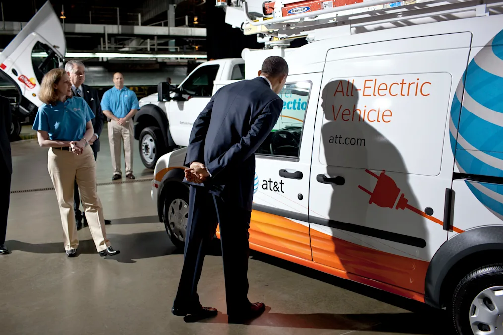 Barack Obama a black golden skin tone man wearing a deep blue suit looking into the window of an AT&T truck