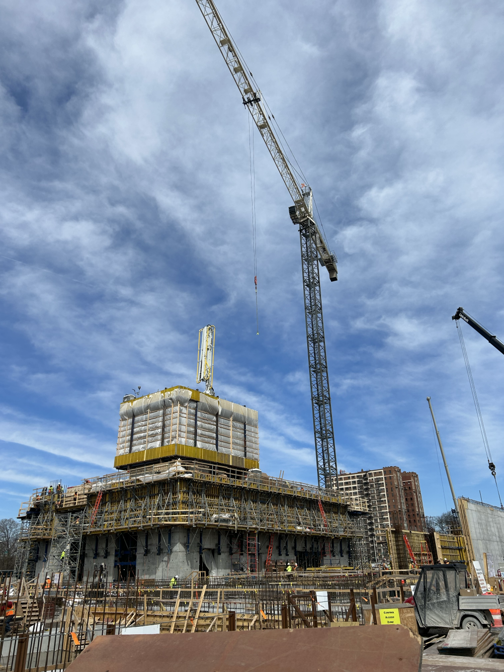 A construction crane towers over a building site with a partially built building. The sky is deep blue with wispy clouds.