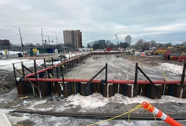 A snowy, muddy construction site with the rectangular outline of metal and red pipe.