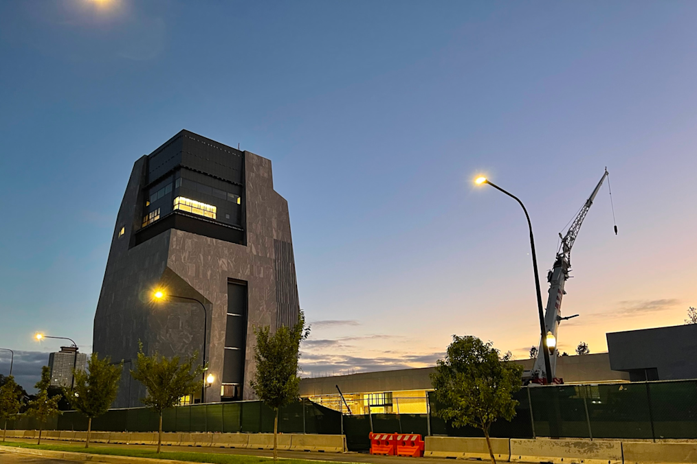 A look at the exterior of the Obama Presidential Center Museum at night. The building is dark gray and has several lights shining from the inside.