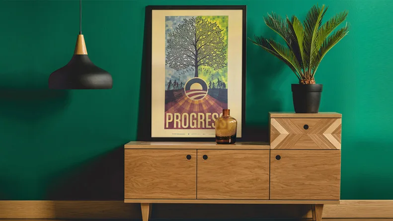 A blue, green, and brown poster with a tree, Obama Rising Sun logo, and "Progress" rests on top of a light brown storage console