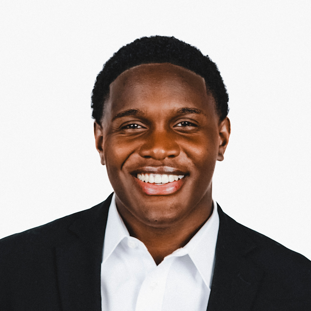 Matthew Dormus, a man with a dark skin tone, smiles at the camera. He is wearing a navy suit and white shirt.