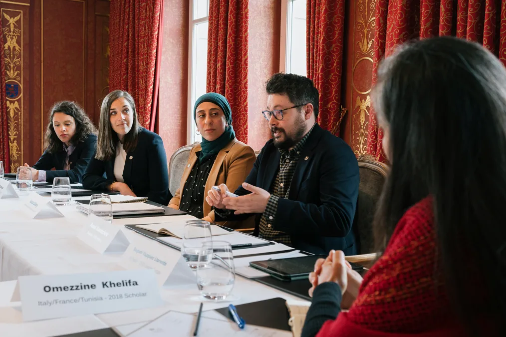 Pavel Kounchev, a man with a light medium skin tone, speaks at the Berlin Roundtable. He is wearing glasses and has short black hair. He sits next to four others with a range of light to medium skin tones.