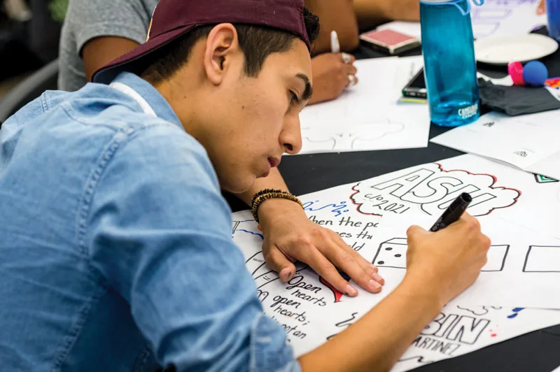 A young man wearing a ball cap draws on paper during an Obama Foundation Training Day in 2017.