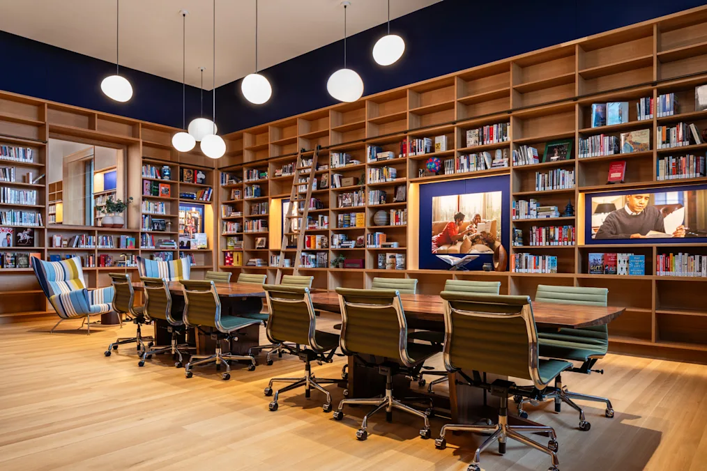 A room with ceiling height bookshelves, a conference table with several empty chairs, and several light fixtures dangling from the ceiling.