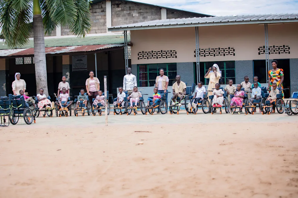 A group shot of Arlette Irankunda, a Black woman with a dark skin tone and blonde braids, and other workers and patients in wheelchairs outside of a physiotherapy clinic.
