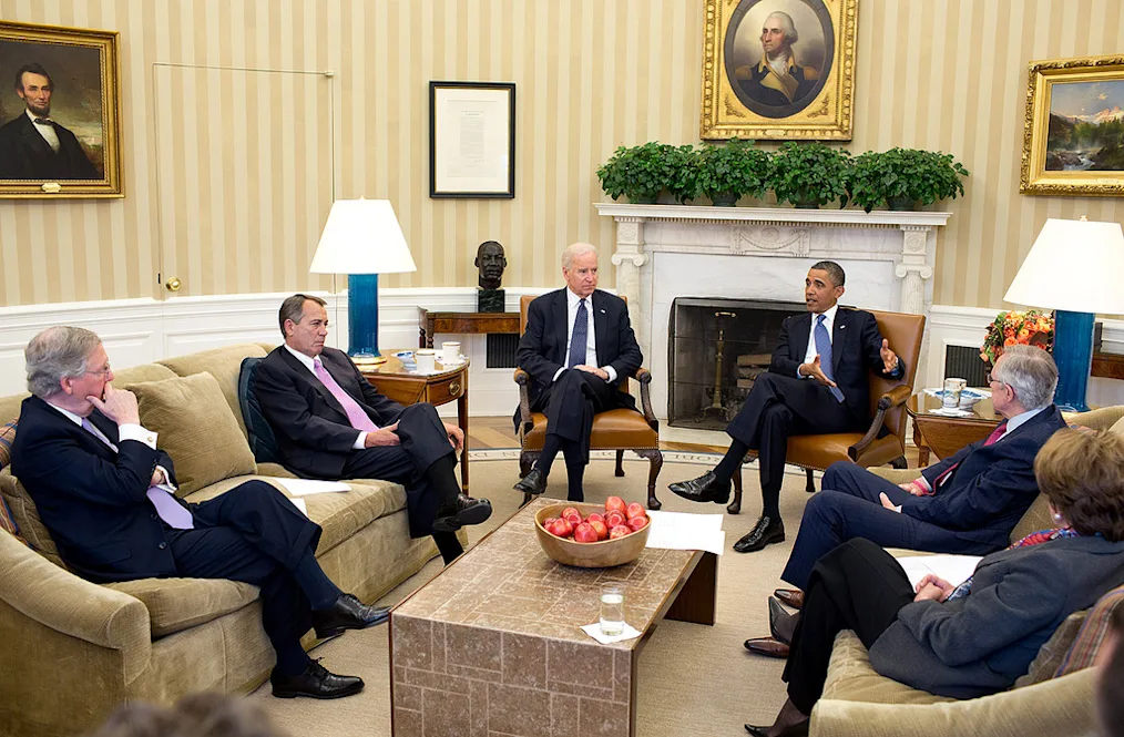 President Obama talks to a group of people with light skin tones in the oval office.