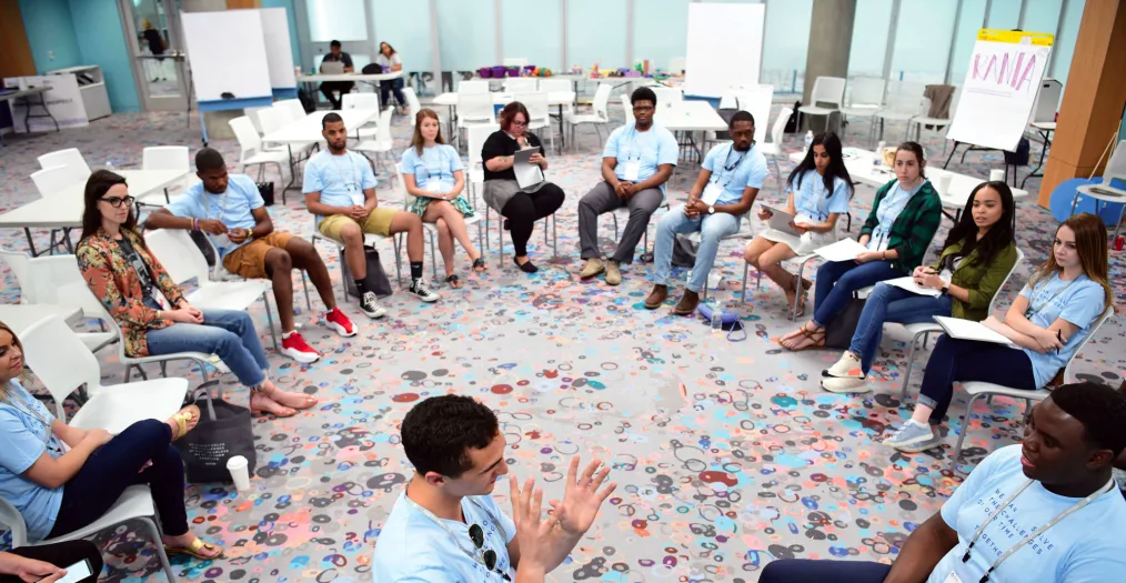 A group of Community Leadership Corps participants sit in a circle engaged in conversation.