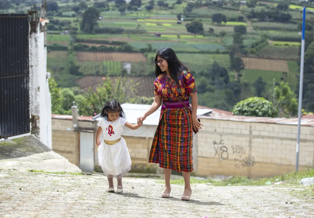 Ancela Ortiz holds her young daughters hand with pastures in the background.