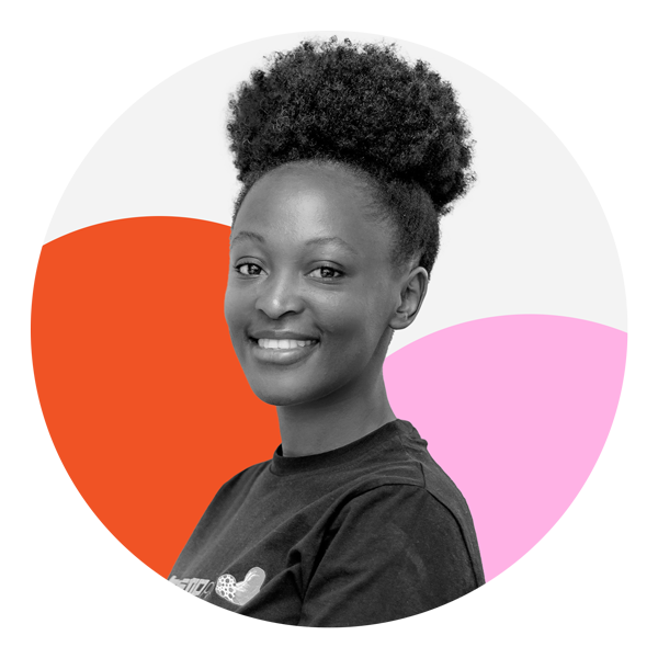 A Black woman with an afro puff hairstyle is facing the camera smiling with her teeth showing. She is wearing a dark colored t-shirt. The photo is black and white and the background features two circles, one which is orange and the other pink. 