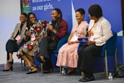 A panel of five women physicians smile on stage as they speak to the crowd of leaders during the Alliance’s Chicago convening. The women have a range of light to dark skin tones, and are wearing blazers and dresses.