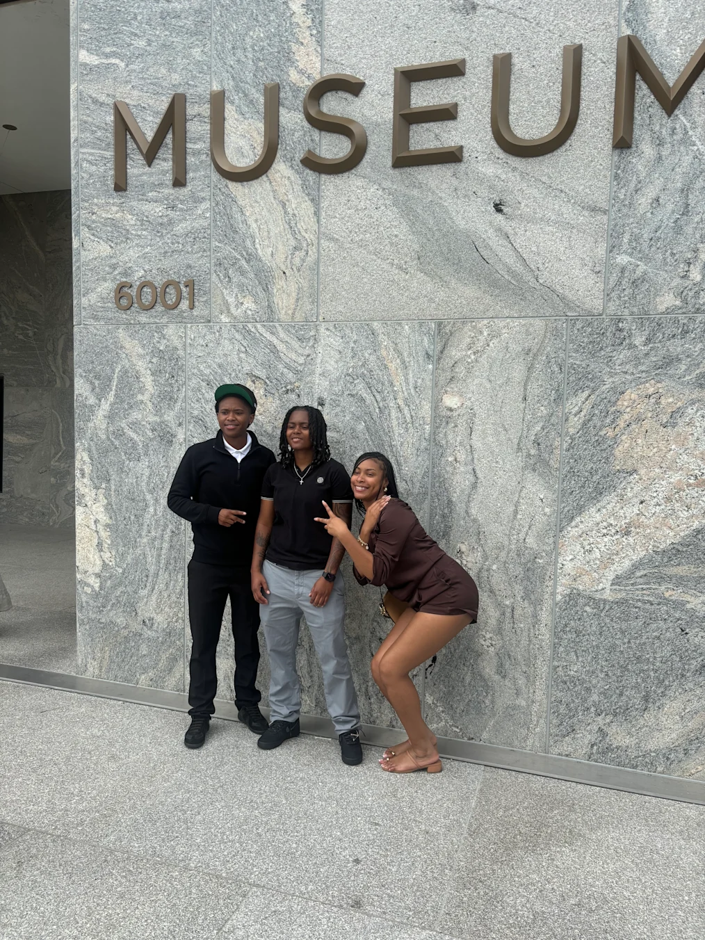 Toryn Parks, a Black woman with a medium skin tone and locs, poses with her siblings in front of the Obama Presidential Center Museum Building sign.