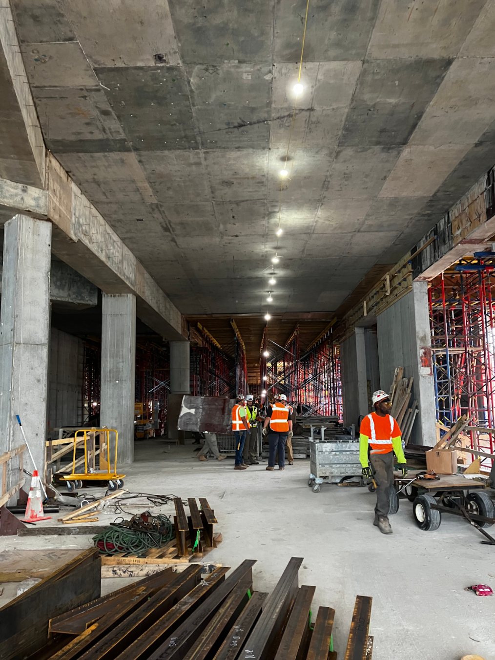 Five workers stand on the platform in the north end of the Hadiya Pendleton Winter Garden. The columns on the left will frame the walls of the auditorium. Construction equipment is scattered throughout the building.