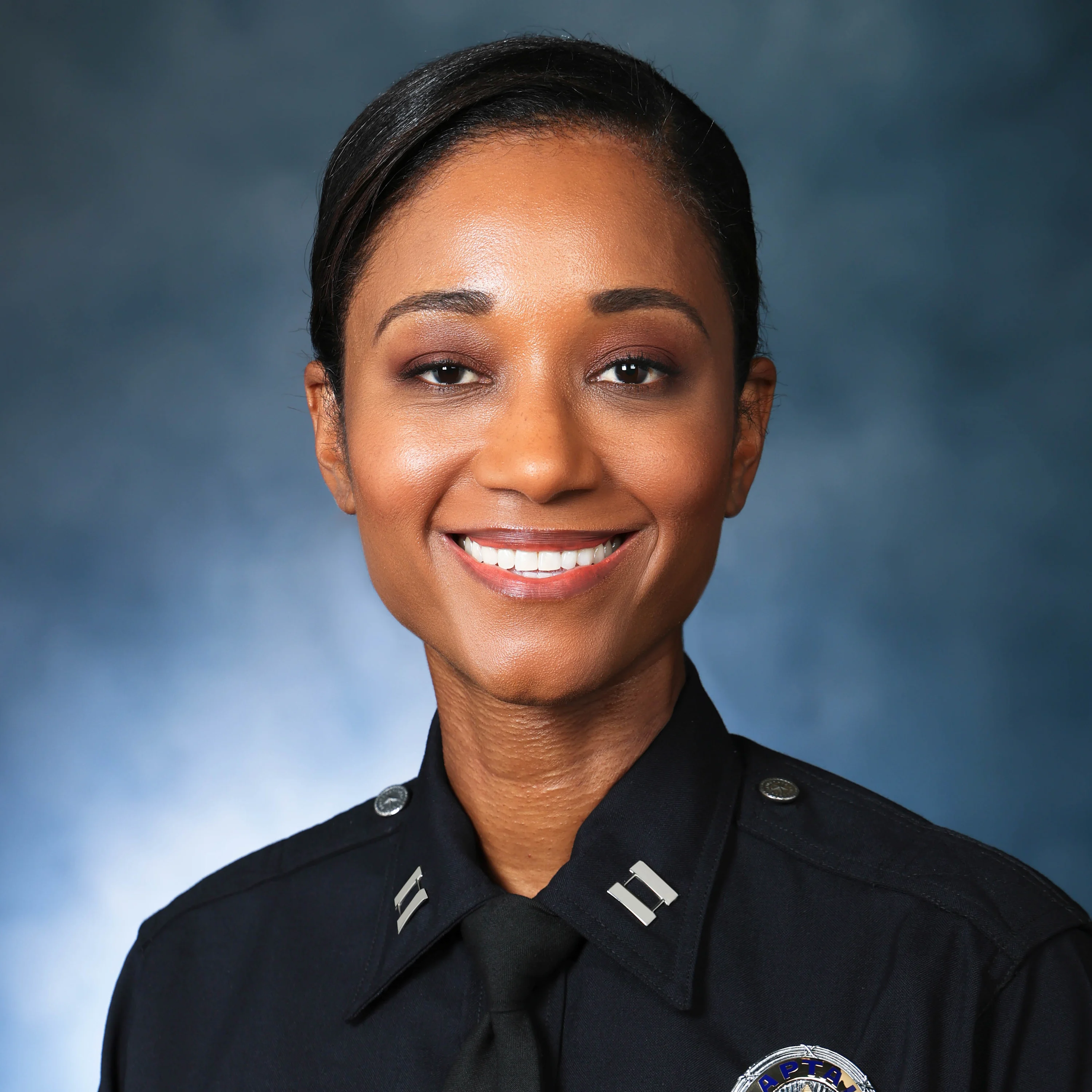 Captain II Shannon White, a Black woman with a medium skin tone, smiles at the camera. Her hair is pulled back. She is wearing a Los Angeles Police Department uniform.