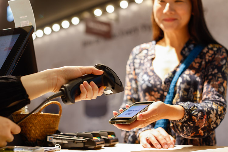 A woman shows her phone to a cashier so they can scan her barcode and qr code.