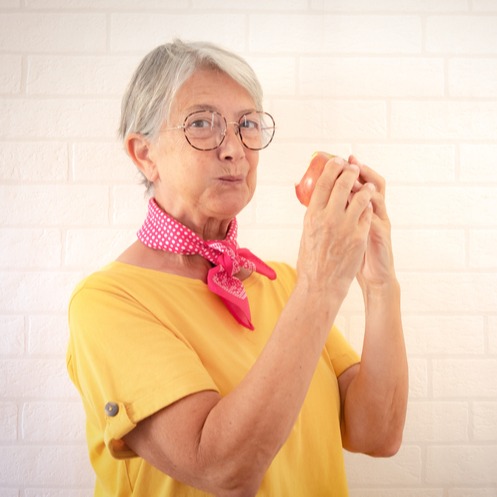 Elderly woman in yellow t-shirt chewing an apple 