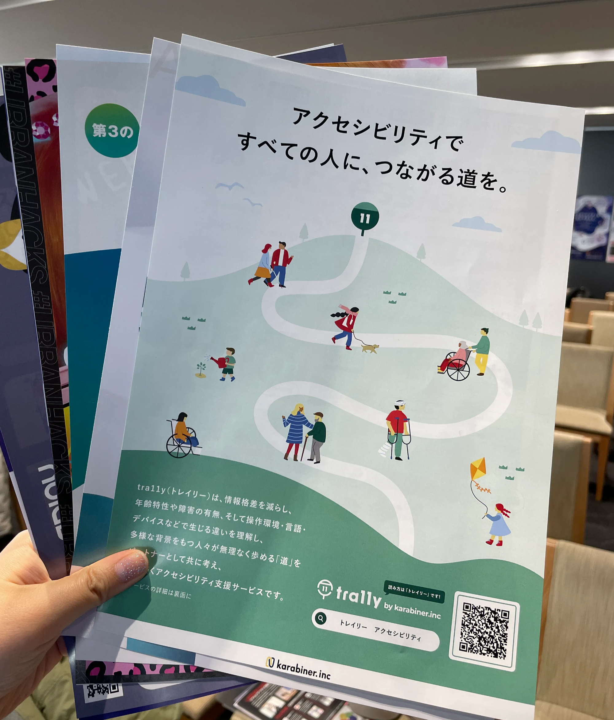 写真:会場でトレイリーのチラシなど配られたチラシ数枚を扇形に広げて左手で持っている様子。