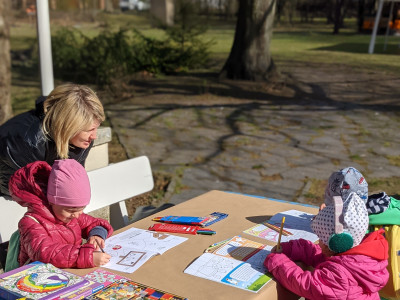 Three kids are playing and drawing together with their mother in the park around Kunsthaus Flora. Image provided by Schlaufuchs e.V.