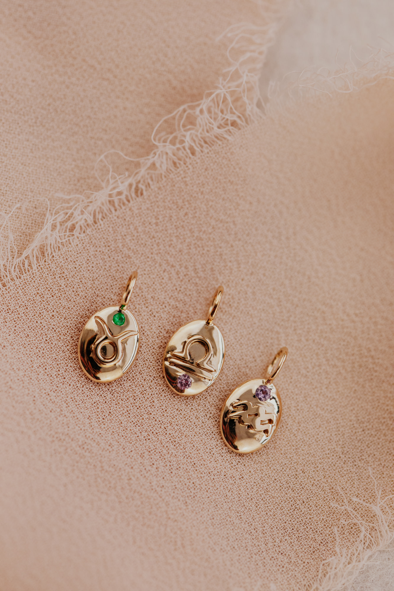 Three gold zodiac charms on a pink surface.