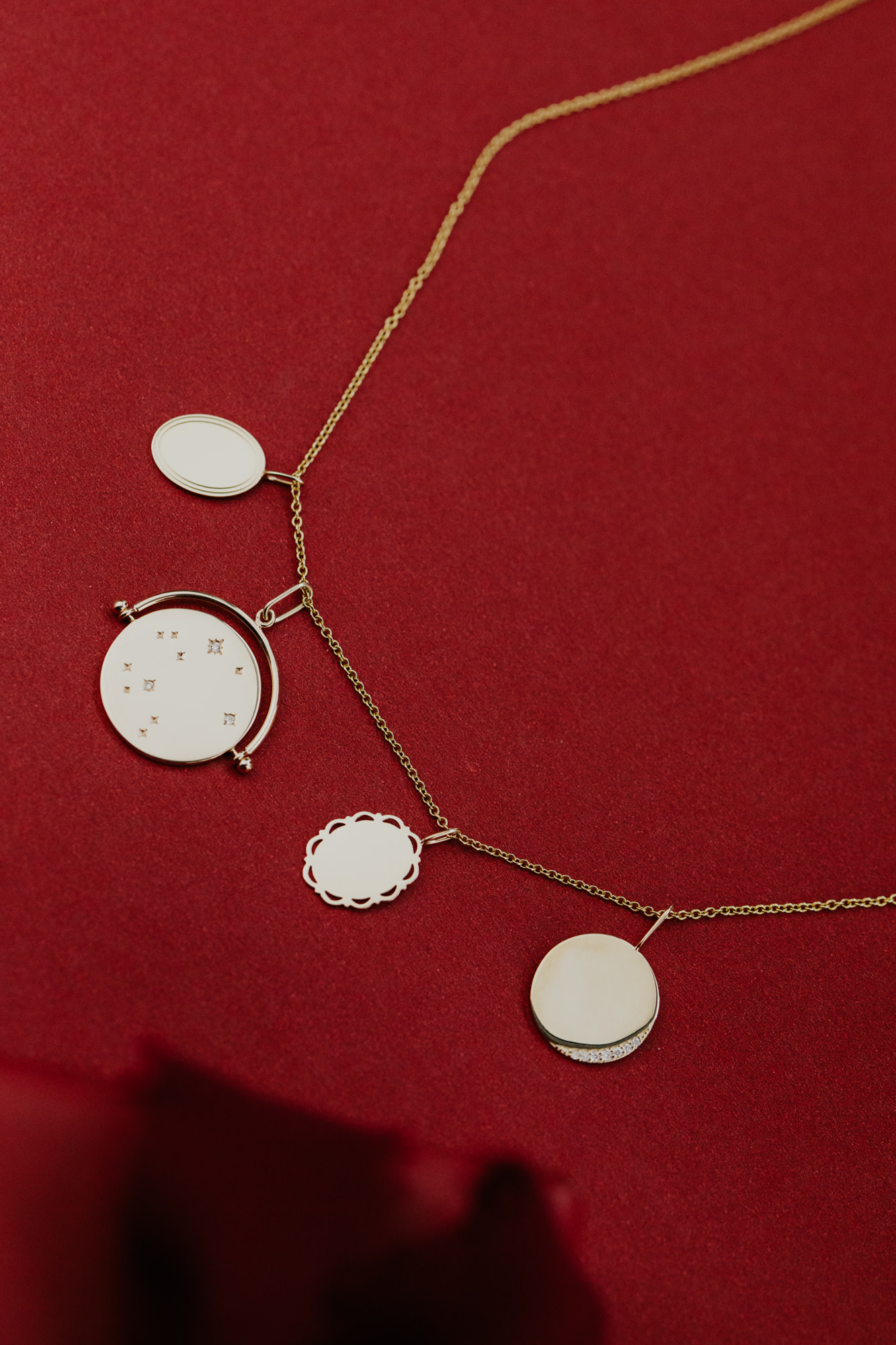 Four gold engravable charms on a gold chain with a red background.