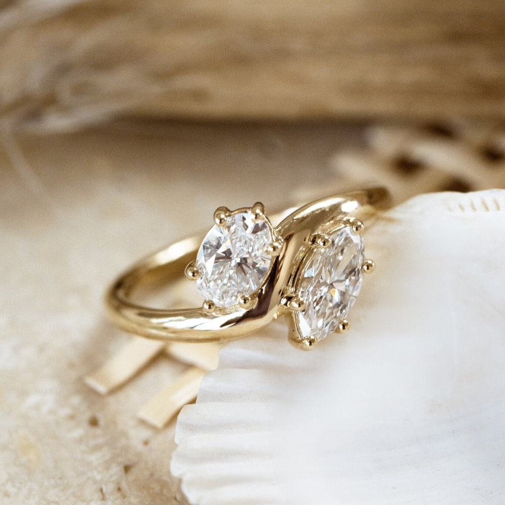 The Harmony toi et moi style engagement ring with an oval and marquise diamond set in prongs, displayed on a seashell.