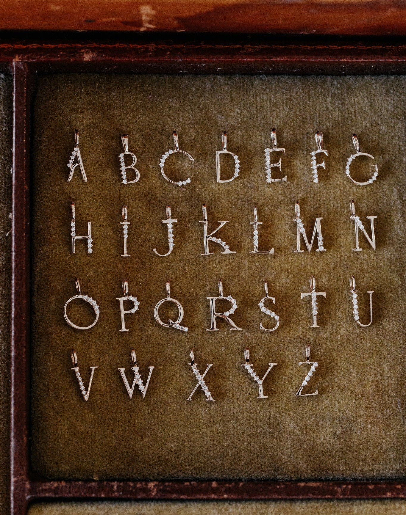 A collection of gold initial pendants in various fonts displayed on a velvet surface.