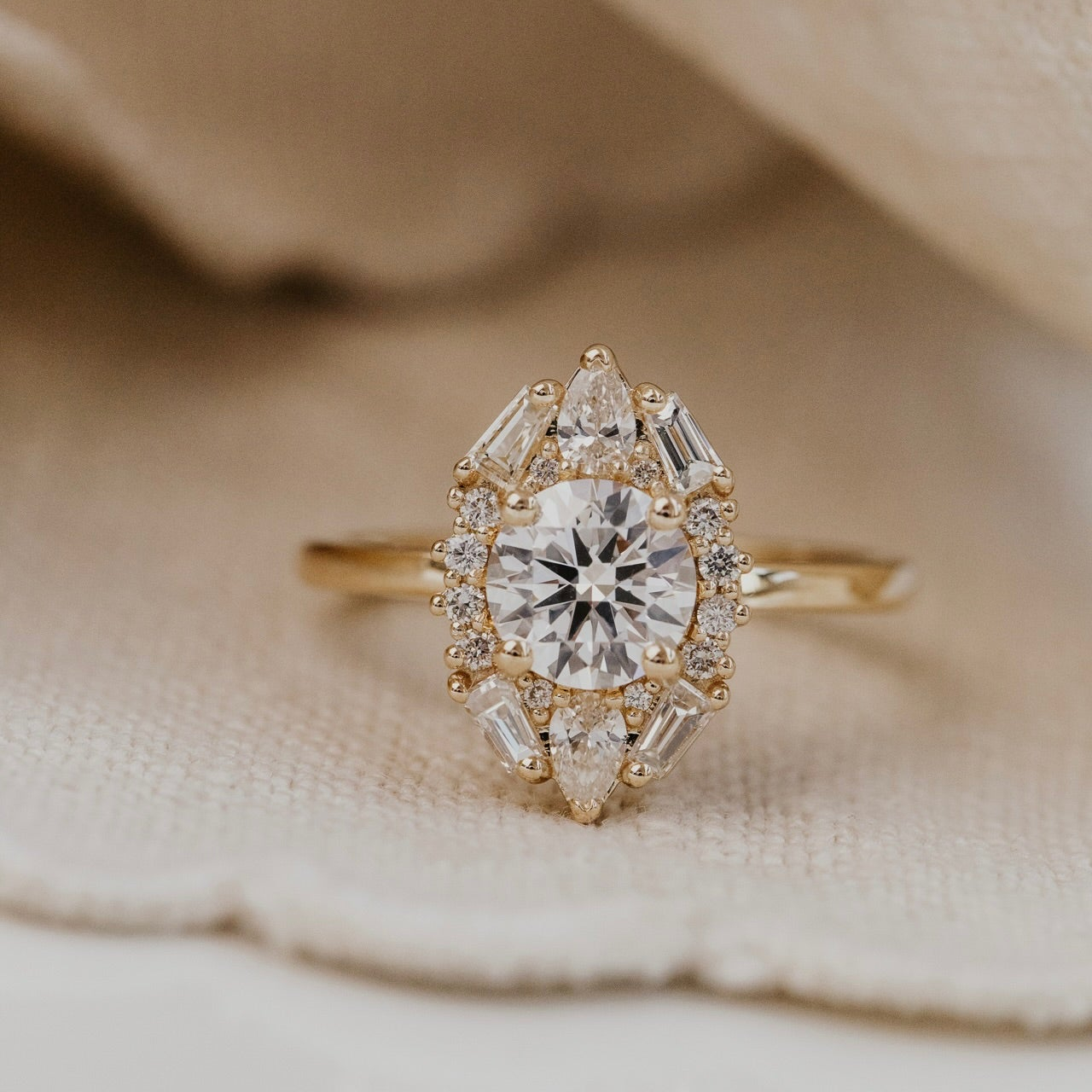 The Lori round diamond ring with a diamond halo on a beige fabric background