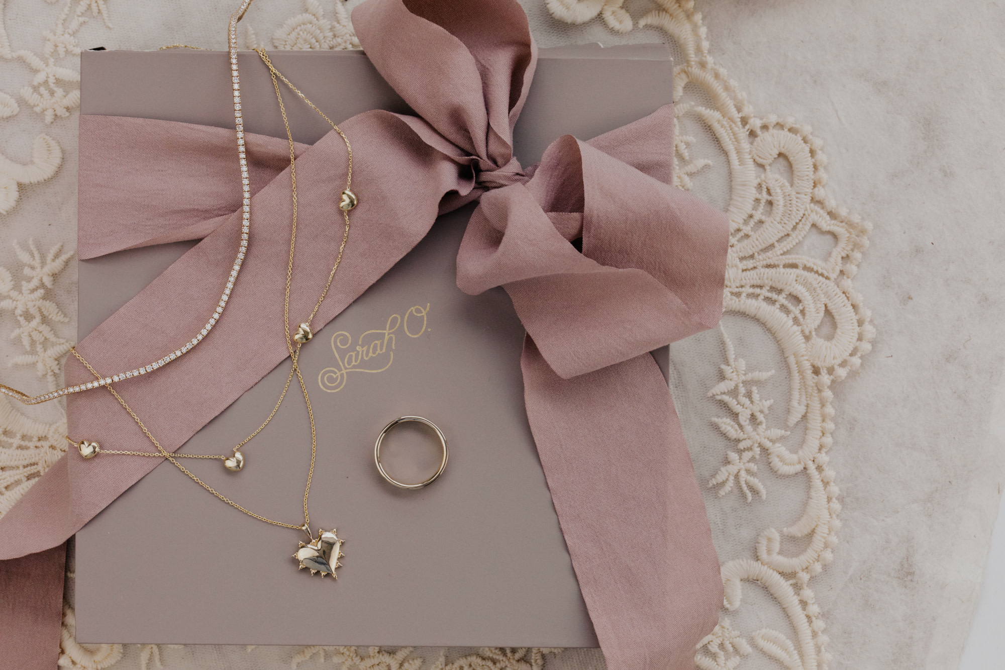 A mis of fine jewelry necklaces and rings laid on a Sarah O. gift box with a blush ribbon.