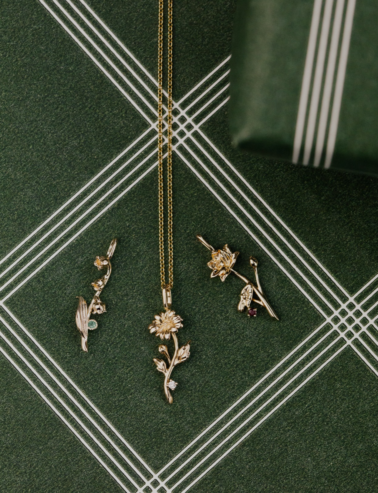 Three gold birth flower charms on a green surface.
