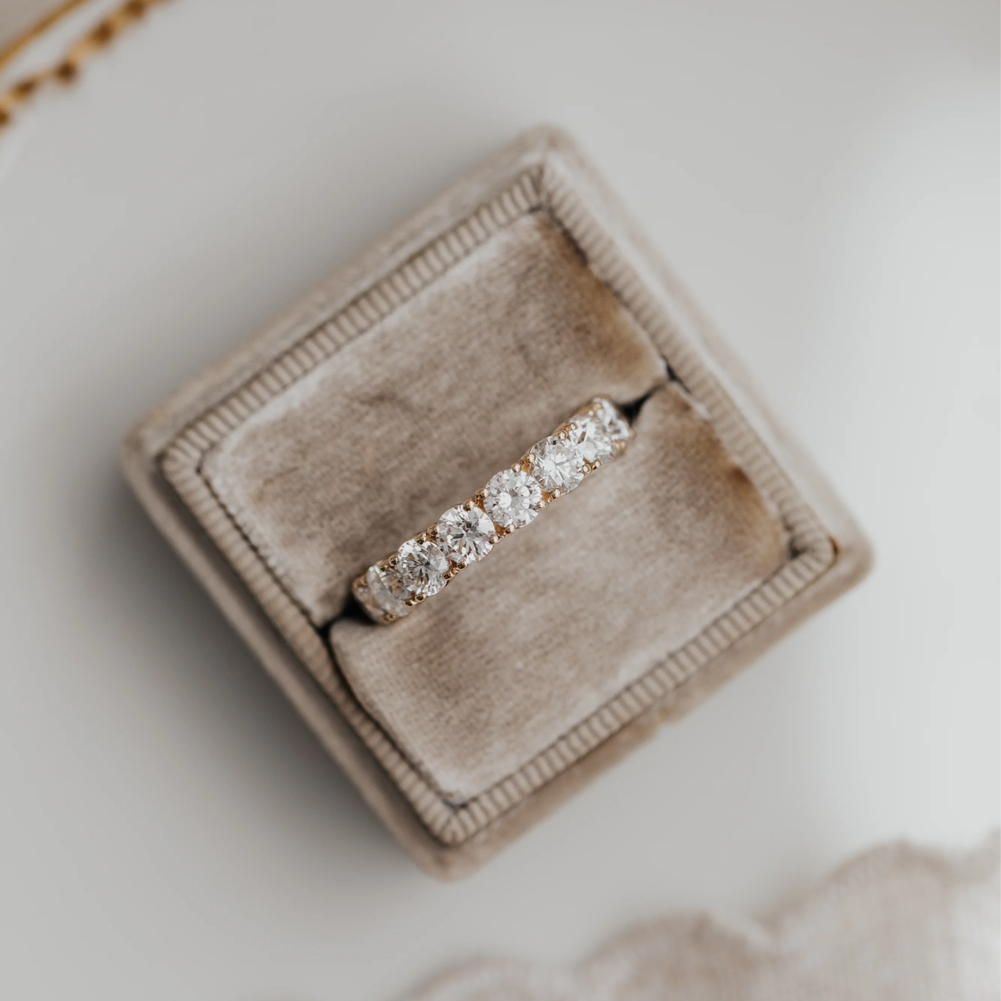 The amara round diamond wedding band in a brown velvet box on a white marbled surface.
