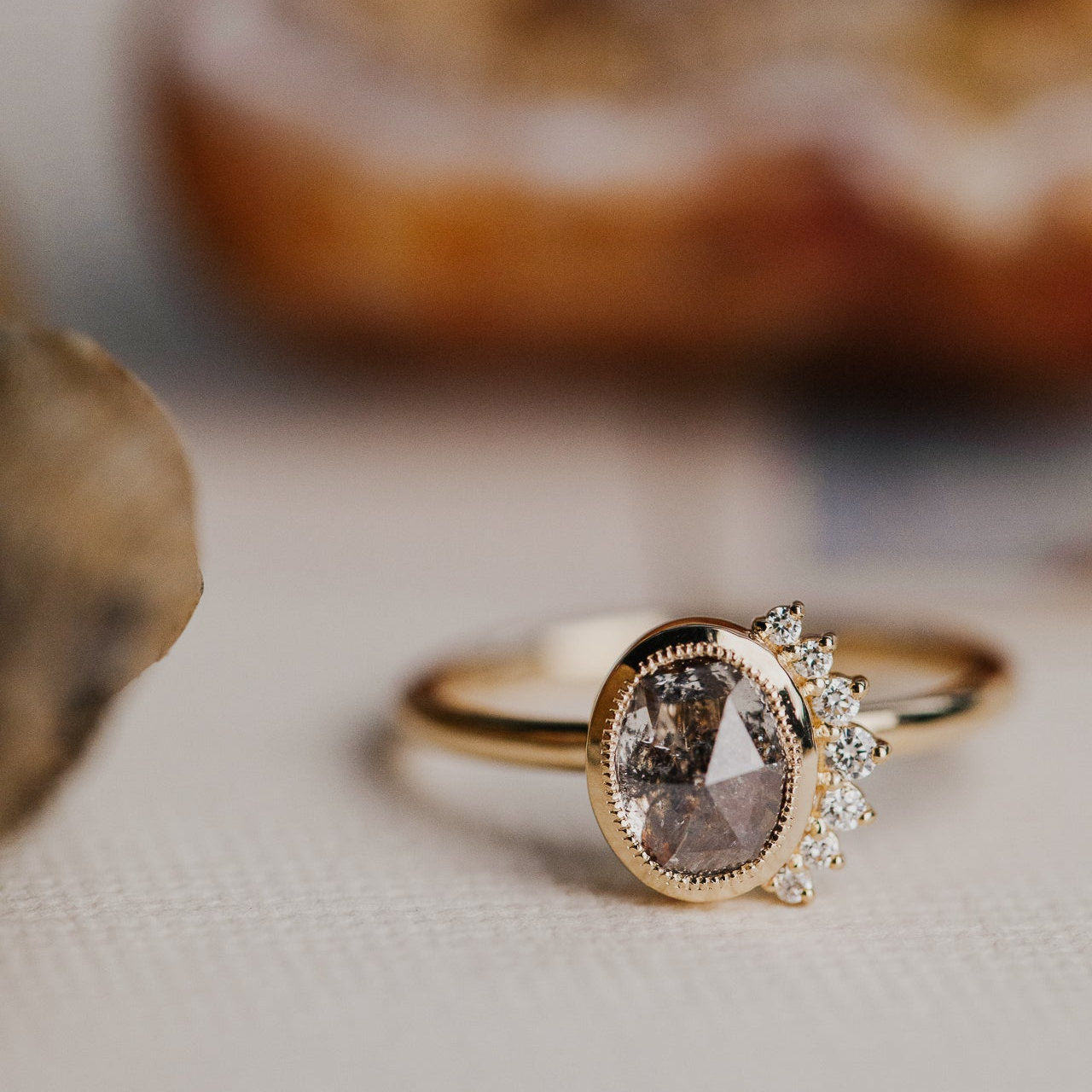 Gold ring with a central oval rustic diamond gemstone and diamond side flare on a neutral background.