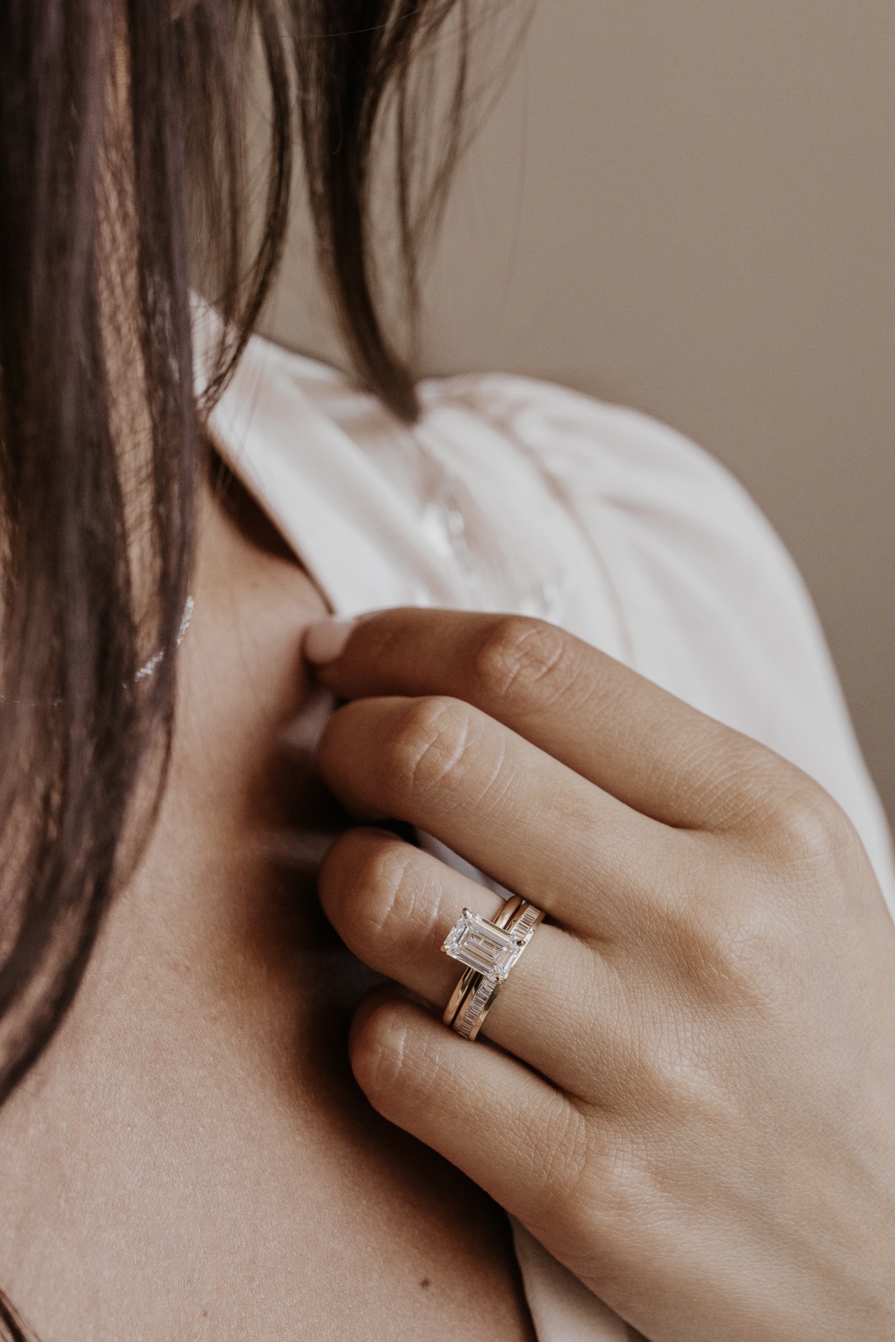 A close up of a person wearing a emerald cut diamond engagement ring with a diamond wedding band.