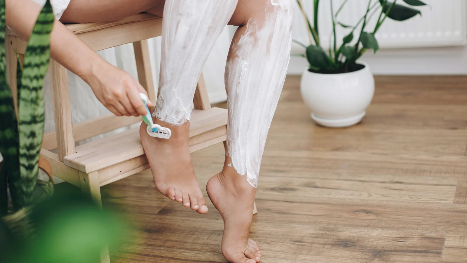 Mulher com gel de barbear aplicado nas pernas fazendo a barba com lâmina de Vênus